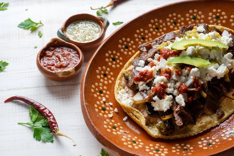 Huarache topped with grilled meat, cheese, avocado, and salsa, from El Huarache’s website